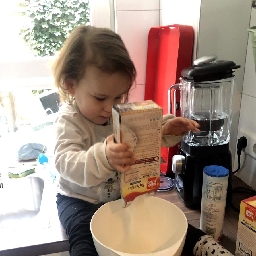 Vida als peuter op het aanrecht, ze giet poffertjesmix in een kom